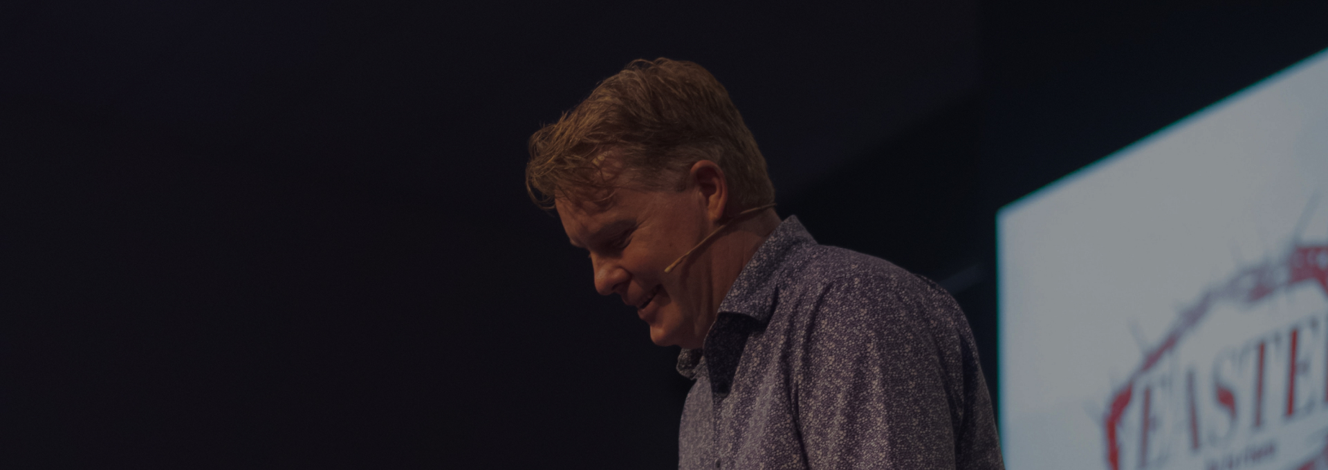 Man in front of screen with microphone in front of a crowd